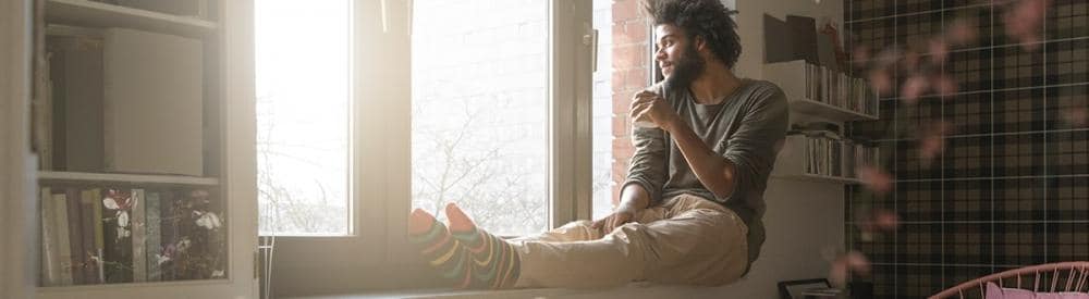 man sitting with his legs up on a windowsill drinking coffee