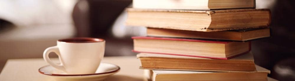 a stack of books next to a coffee cup in a saucer