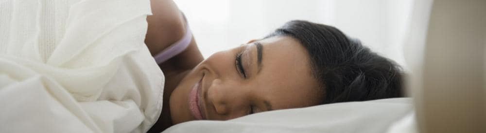 woman laying in bed smiling under bed sheets