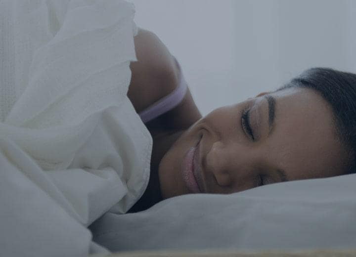 woman laying in bed smiling under bed sheets